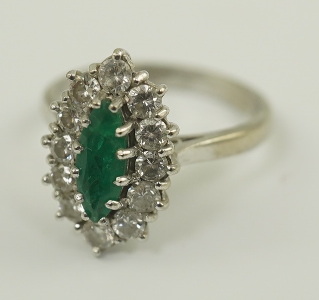 A modern 18ct white gold and single stone marquise cut emerald set ring, bordered with round brilliant cut diamonds